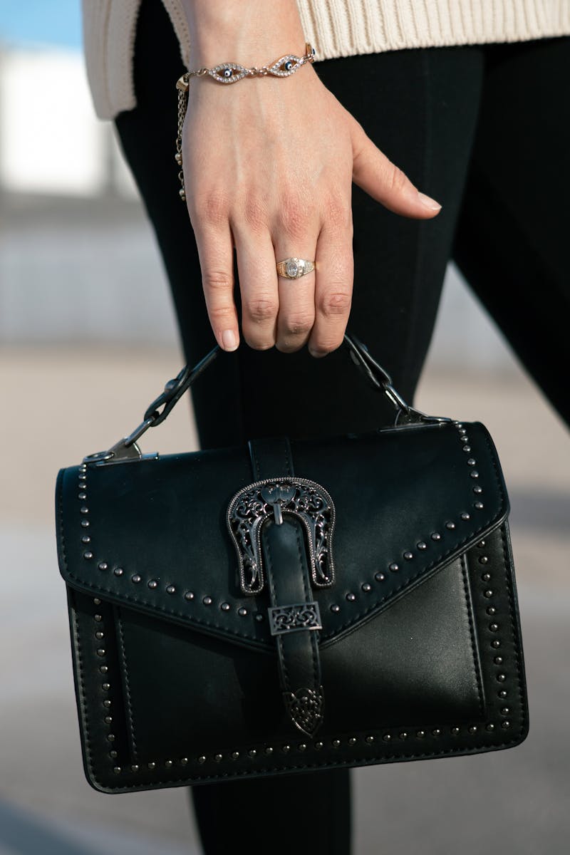 Close-up of a woman's hand holding a chic black handbag with stud details outdoors.