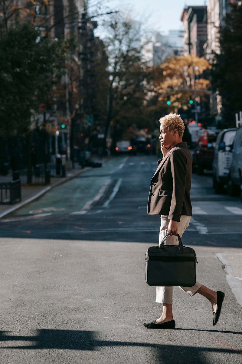 Young professional woman crossing city street with briefcase on a sunny day.